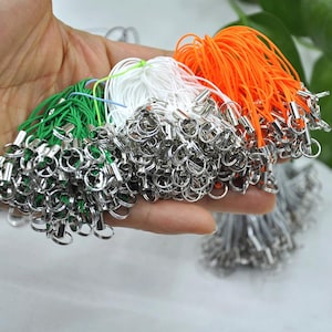 May include: A hand displays several bundles of colourful lanyards. Each lanyard has a silver-coloured metal ring and a cord in various colours, including green, white, and orange. The lanyards are bunched together, with the metal rings visible.