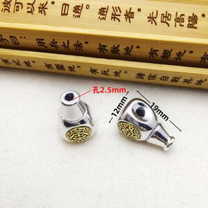 May include: Two silver-colored metal beads with a gold-colored filigree design. Each bead has a hole of 2.5mm, is 12mm high, and 19mm wide. The beads are on a light-colored surface.