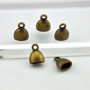 May include: Five antique gold-toned metal end caps for cords or jewelry making. The end caps have a rounded top and a small loop at the top.
