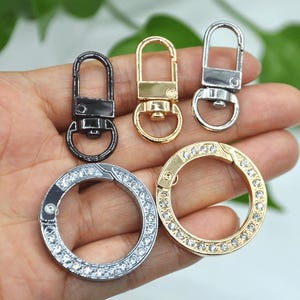 May include: Four different metal keychains, including two silver swivel clasps with rhinestones, a gold swivel clasp with rhinestones, and a black swivel clasp.