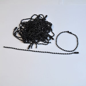 Puede incluir: Un montón de cadena de metal negro con una sola cadena extendida hacia la derecha. La cadena está hecha de pequeños eslabones redondos.