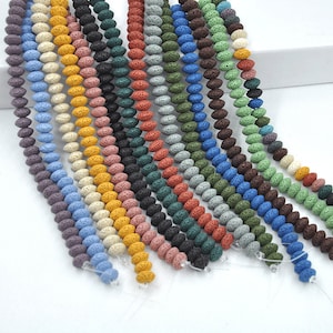 Puede incluir: Surtido de cuentas de roca volcánica en varios colores, incluyendo azul, verde, marrón, amarillo y rojo. Las cuentas son de forma ovalada y tienen una textura porosa.