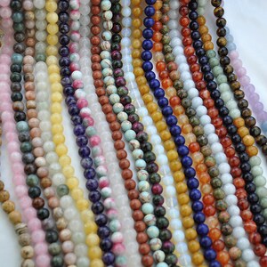Puede incluir: Surtido de cuentas de piedras preciosas de colores, incluyendo amarillo, verde, azul, rojo y marr&oacute;n. Las cuentas son redondas y lisas, y est&aacute;n dispuestas en filas.