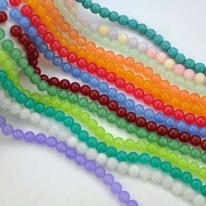 Puede incluir: Una colecci&oacute;n de 14 hebras de cuentas redondas, opacas, con acabado mate, en varios colores, incluyendo turquesa, azul claro, lavanda, blanco, verde, naranja y rojo. Las cuentas est&aacute;n enhebradas sobre un fondo blanco.