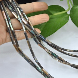 May include: Strands of iridescent, rectangular beads in shades of brown, gray, and hints of blue and green. The beads are strung together, creating a necklace or bracelet design. The beads have a polished, reflective surface.