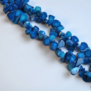 May include: Close-up of two strands of blue gemstone beads. The beads are irregularly shaped, with a mix of light and dark blue hues. The beads are strung together, creating a necklace or bracelet.