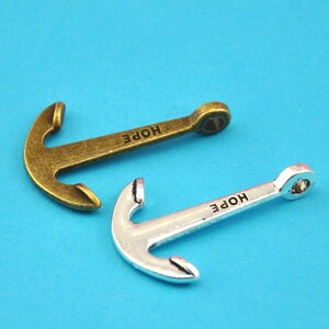 May include: Two metal anchor charms, one bronze-toned and one silver-toned, each with the word "HOPE" engraved on the shaft. The anchors are set against a bright blue background, ideal for jewelry making or nautical-themed crafts.