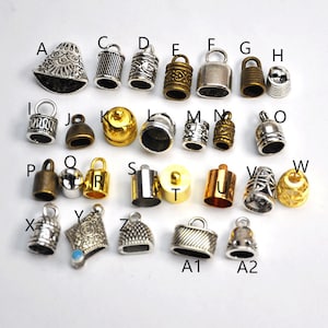 May include: Assortment of 26 silver and gold metal end caps for jewelry making. The end caps are in various shapes and sizes, including round, oval, square, and bell-shaped.