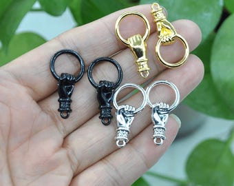 Könnte beinhalten: Vier verschiedene Schlüsselanhänger aus Metall mit einem Handdesign. Zwei sind silber, einer ist gold und einer ist schwarz.