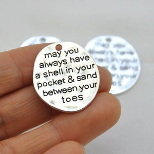 May include: Silver charm with the text "may you always have a shell in your pocket & sand between your toes".