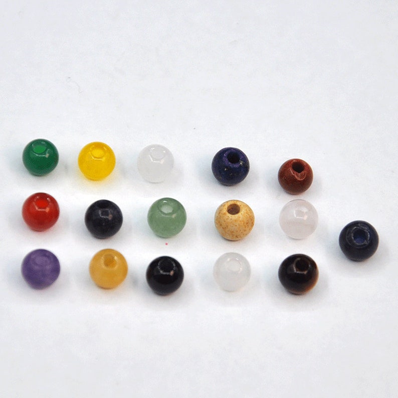 May include: Assortment of 15 round gemstone beads in various colors, including green, yellow, white, blue, red, purple, and brown. The beads are approximately 1 cm in diameter and have a smooth, polished finish.