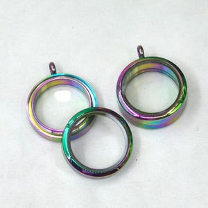 Puede incluir: Tres colgantes de medall&oacute;n de metal iridiscente con inserciones de vidrio transparente. Los medallones son redondos y tienen un acabado brillante.