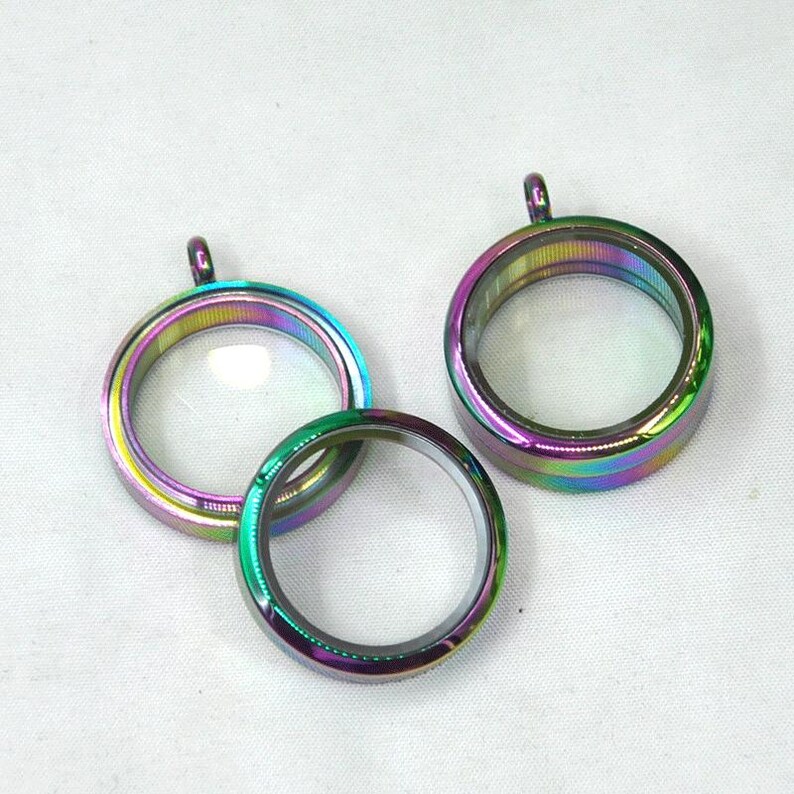 Puede incluir: Tres colgantes de medall&oacute;n de metal iridiscente con inserciones de vidrio transparente. Los medallones son redondos y tienen un acabado brillante.