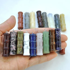 May include: A collection of 12 gemstone pendants in the shape of bamboo. The pendants are made of various stones, including red jasper, green aventurine, white marble, lapis lazuli, rose quartz, green jade, tiger's eye, amethyst, and more.