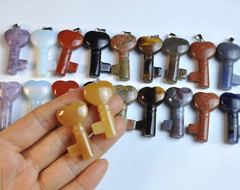 Op de afbeelding: Assortiment van edelsteen sleutel hangers in verschillende kleuren, waaronder amethist, opaal, rode jaspis, zwarte obsidiaan, tijgeroog en meer. De sleutels zijn gemaakt van natuursteen en hebben een hartvormige bovenkant.