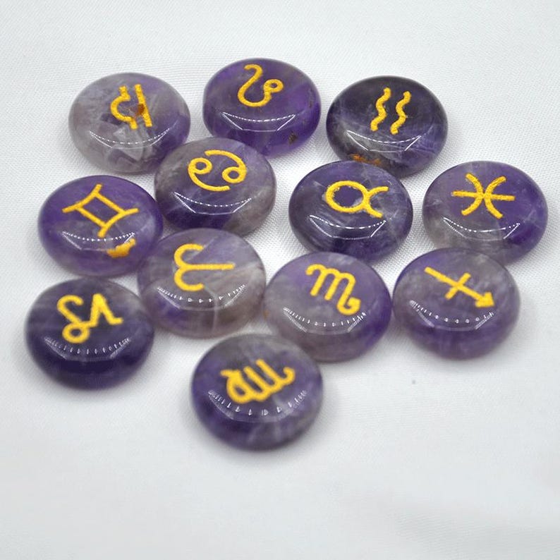 May include: Twelve amethyst gemstone tumbled stones with gold zodiac symbols. The stones are arranged in a circle on a white background.