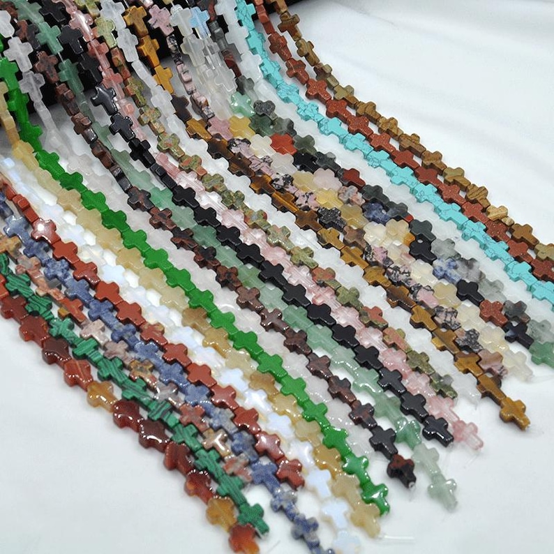 May include: A strand of gemstone beads in various colors and patterns, each bead is shaped like a cross. The beads are strung on a clear thread and are ready to be used for jewelry making.