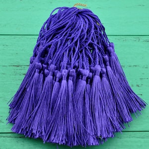 Puede incluir: Un montón de borlas moradas hechas de hilo. Las borlas están atadas juntas en la parte superior y cuelgan en un manojo suelto.