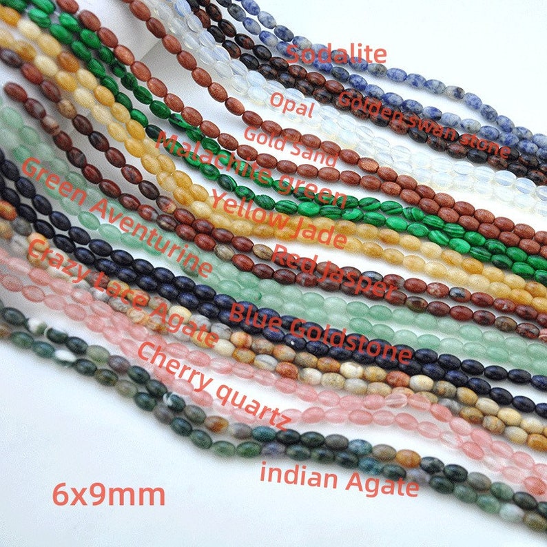Pu&ograve; includere: Assortimento di 16 fili di perle di pietre preziose di forma ovale, ogni filo misura 6 mm per 9 mm. Le perle sono disposte in file, con i nomi di ogni tipo di pietra preziosa etichettati sotto ogni fila. Le pietre preziose includono: sodalite, opale, sabbia dorata, giada gialla, diaspro rosso, aventurina verde, agata a pizzo pazzo, goldstone blu, quarzo ciliegia e agata indiana.