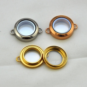 May include: Three silver and gold locket charms with clear glass inserts. The charms have a round shape and are designed to be used for jewelry making.