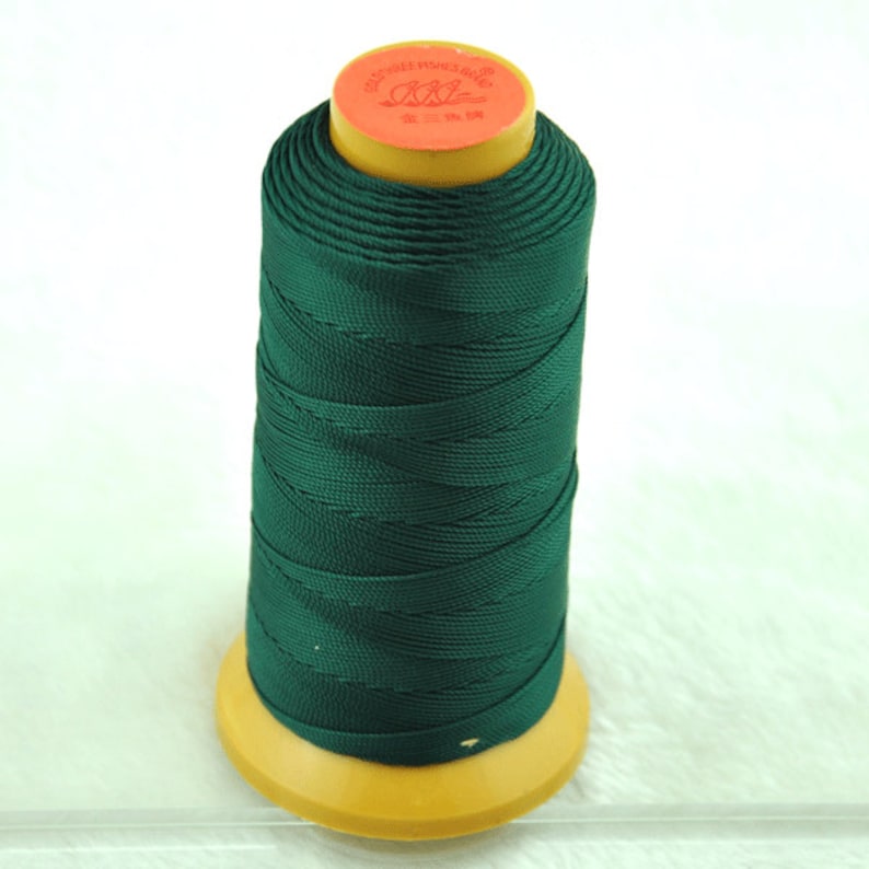 May include: A spool of dark green thread with a yellow base and top. The top of the spool has red and gold text. The thread is tightly wound, creating a cylindrical shape. The thread is likely used for sewing or crafting.