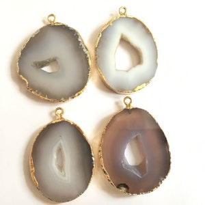 May include: Four agate slice pendants with gold-plated edges. Each pendant features a unique, naturally occurring hole in the center. The agate is a light gray color with a white center.