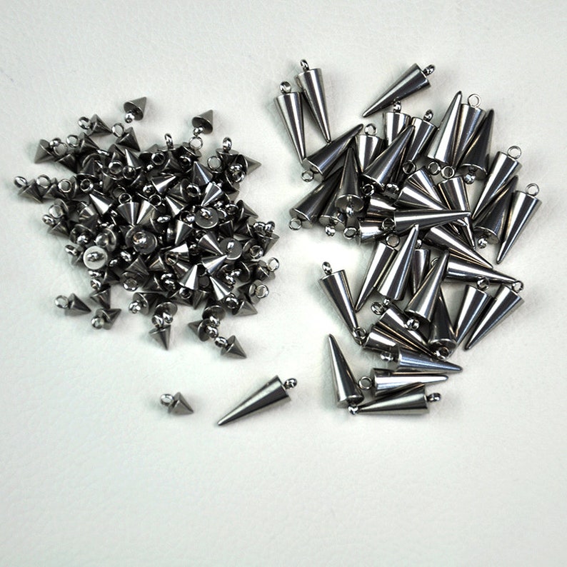 Puede incluir: Dos pilas de tachuelas de metal plateado en forma de cono con un bucle en la parte superior. Las tachuelas est&aacute;n dispuestas en un patr&oacute;n aleatorio.