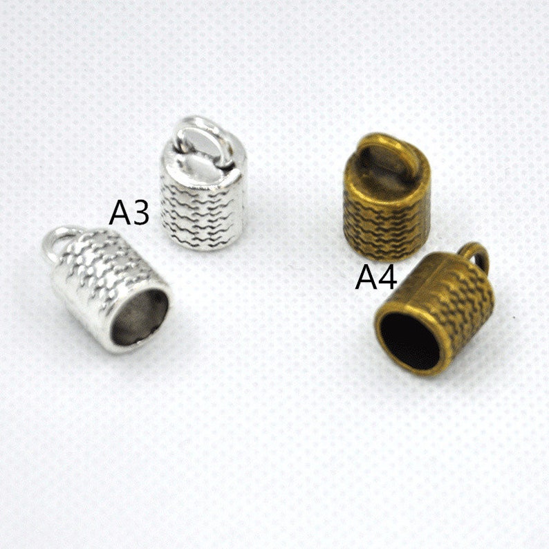 May include: Two metal cord end caps, one silver and one gold, with a textured design and a loop at the top. The silver cap is labeled "A3" and the gold cap is labeled "A4".