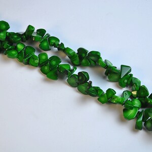 May include: Two strands of bright green, irregularly shaped beads. The beads have a glossy finish and appear to be made of a polished material. The beads are arranged in a flowing, organic pattern against a white background. The beads are a vibrant shade of green.