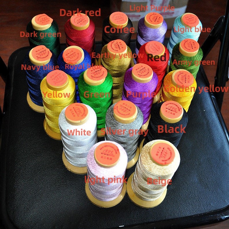 May include: A collection of colorful spools of thread, including dark red, navy blue, yellow, white, and black. Each spool is labeled with its color name. The threads are neatly arranged, showcasing a variety of hues for sewing and crafting projects.