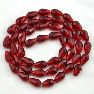 May include: A strand of red faceted teardrop glass beads. The beads are strung on a clear thread.