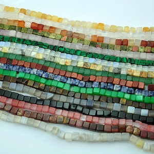 Può includere: Assortimento di perline quadrate di pietre preziose di vari colori, tra cui verde, rosso, blu, marrone e bianco. Le perline sono disposte in file, creando un motivo visivamente accattivante.