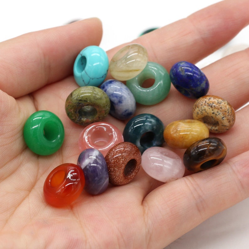 May include: Assortment of donut-shaped gemstone beads in various colors, including green, blue, pink, red, and brown. The beads are made of natural stones and have a smooth, polished finish.