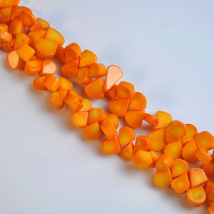 May include: Close-up of a necklace made of bright orange, irregularly shaped beads. The beads have a glossy finish and are strung together, creating a vibrant and eye-catching accessory. The necklace is set against a white background.