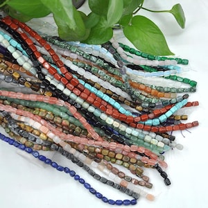 Può includere: Una collezione di perline di pietre preziose colorate, ogni perlina ha una forma quadrata. Le perline sono infilate su fili di diverse lunghezze. Le perline sono un mix di colori, tra cui rosso, verde, blu, marrone e bianco.