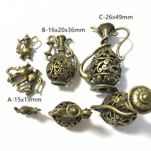 May include: A collection of antique bronze-colored decorative metal pieces. The pieces include small teapots, vases, and a decorative sphere. The largest piece is a vase measuring 26mm x 49mm. The pieces have intricate openwork designs.
