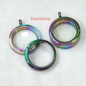 Puede incluir: Tres colgantes de medall&oacute;n de metal iridiscente arco&iacute;ris con inserciones de vidrio transparente. Los medallones tienen un bucle en la parte superior para sujetarlos a una cadena.