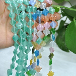 Puede incluir: Hileras de cuentas de piedras preciosas de colores en varias formas y colores, incluyendo verde, azul, rosa y amarillo. Las cuentas est&aacute;n ensartadas, creando una exhibici&oacute;n vibrante y llamativa. Las cuentas se sostienen en una mano.