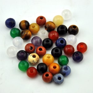 May include: A collection of colorful gemstone beads, including green, red, blue, purple, brown, white, and yellow. The beads are round and have a smooth, polished finish.