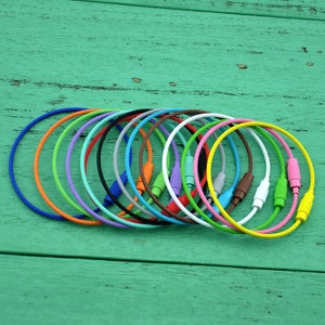 May include: A collection of 15 colorful cable keychains with metal loops. The keychains are arranged in a row on a green wooden surface. The colors include blue, green, yellow, orange, red, purple, pink, white, gray, and black.