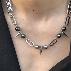 Puede incluir: Un collar de cadena plateada con cuentas negras y p&uacute;as plateadas. La cadena es una cadena gruesa de curb con un dise&ntilde;o de eslab&oacute;n &uacute;nico.