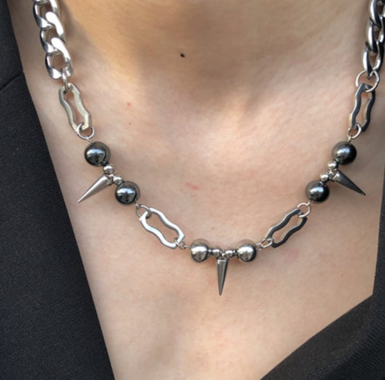Puede incluir: Un collar de cadena plateada con cuentas negras y p&uacute;as plateadas. La cadena es una cadena gruesa de curb con un dise&ntilde;o de eslab&oacute;n &uacute;nico.