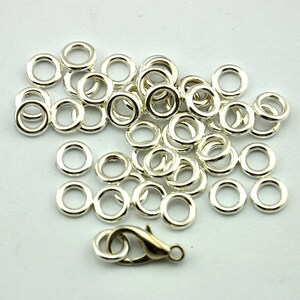 May include: A pile of silver jump rings, approximately 50 pieces, with a silver lobster clasp.