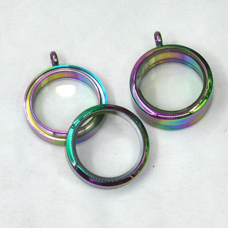 Puede incluir: Tres colgantes de medall&oacute;n de metal iridiscente con inserciones de vidrio transparente. Los medallones son redondos y tienen un acabado brillante.