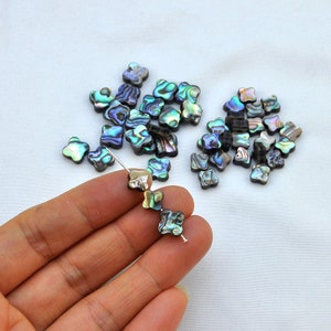 May include: A pile of iridescent abalone shell beads in the shape of a four-leaf clover. The beads are strung on a silver wire.