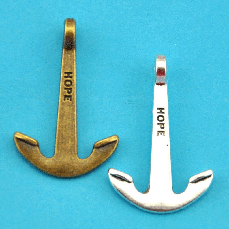 May include: Two anchor charms, one bronze-toned and one silver-toned, against a blue background. Each anchor has the word "HOPE" printed vertically on the shaft. The anchors are designed with a loop at the top for attaching to a chain or other jewelry.