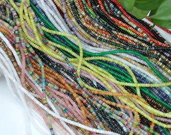 Puede incluir: Una colección de cuentas de piedras preciosas de colores, enhebradas en cordones finos, en varios tonos de verde, azul, rojo, amarillo y blanco. Las cuentas están dispuestas en forma de abanico, mostrando los diferentes colores y texturas.
