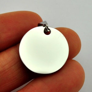 May include: A round, silver-colored pendant with a smooth, polished surface. The pendant has a small hole at the top for attaching a chain or cord.