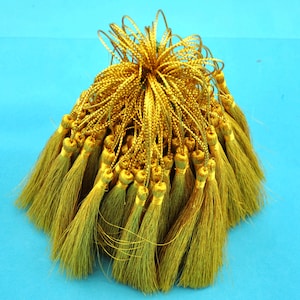 Puede incluir: Un montón de flecos dorados, aproximadamente 50 piezas, con una textura larga, fina y ligeramente deshilachada. Los flecos están atados juntos en la parte superior, creando un haz.