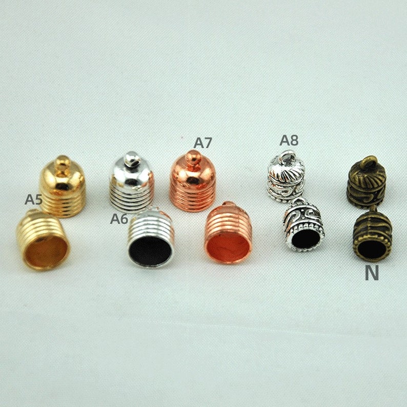 May include: Assortment of 10 metal cord end caps in various finishes, including gold, silver, copper, and bronze. The caps have different designs, including plain, ribbed, and ornate.